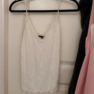 Vit ribbad linnetopp med spetsdetaljer - Säljer en söt vit ribbad linnetopp med spetsdetaljer vid axelbanden och längs v-ringningen. Inga defekter aldrig använd