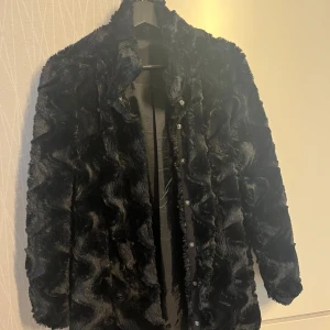 Svart pälsjacka från Vero Moda - Säljer en snygg svart pälsjacka från Vero Moda. Jackan har en cool vågig textur och knäppning framtill. Perfekt för att hålla sig varm och stilren under kyliga dagar. 🖤