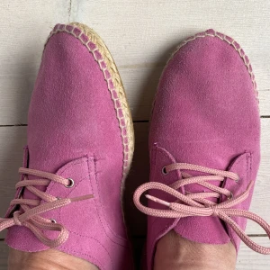 Rosa mockaskor med snörning - Väldigt söta glassrosa mockaskor med snörning i espadrillos-modell.  Skorna har en naturfärgad sula med dekorativa sömmar och kommer från spanska märket Zarshop. Storlek 38. 
