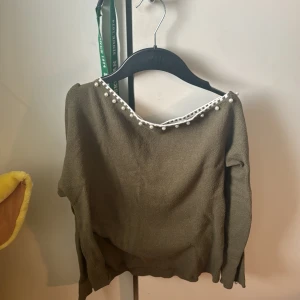 Olivgrön tröja med pärldetaljer - Snygg olivgrön tröja med pärldetaljer längs halsringningen. Tröjan har långa ärmar och en elegant design som passar perfekt för höst och vår. Perfekt för att ge din outfit en stilfull touch. Den är från Shein 