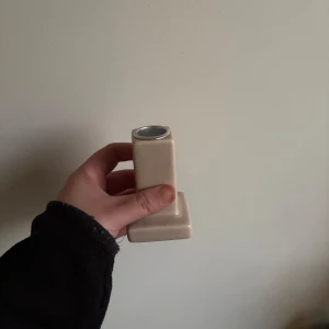 Ljusstake  - Säljer en stilren beige ljusstake med en unik, modern design. Ljusstaken har en rektangulär form med en silverfärgad topp. Perfekt för den som gillar minimalistisk estetik.