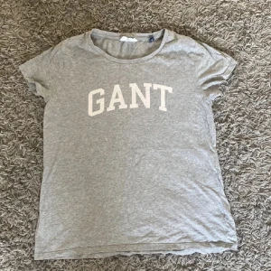 Grå t-shirt från Gant - Säljer en grå t-shirt från Gant med vit logga på bröstet. T-shirten har en rund halsringning och korta ärmar. Använd max 5 gånger!💓