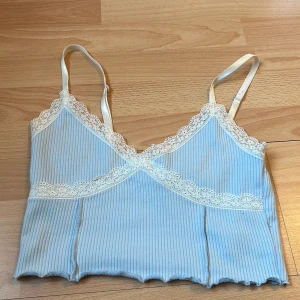 Ljusblå ribbad linnetopp från H&M Divided - Säljer en söt ljusblå ribbad linnetopp från H&M Divided. Toppen har spetsdetaljer vid halsringningen och justerbara axelband. Perfekt för varma dagar eller som ett lager under en tröja.