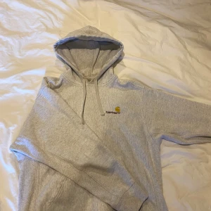 Grå hoodie från Carhartt - Säljer en klassisk grå hoodie från Carhartt med justerbar huva och känguruficka. Perfekt för en avslappnad stil. Den har en liten Carhartt-logga broderad på bröstet.