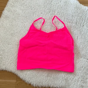 Neonrosa ribbad linnetopp - Säljer en neonrosa ribbad linnetopp med smala axelband. Perfekt för en färgglad och sportig look. Toppen är stretchig och bekväm att bära.