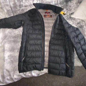 Parajumper Jacka - Säljer en svart superlätt dunjacka från Parajumpers med dragkedja och två fickor framtill. Jackan har en snygg patch på ärmen och är perfekt för kyligare dagar. Den är designad för att hålla dig varm utan att kännas tung.