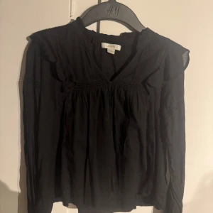 Svart blus från Gina Tricot - Säljer en stilren svart blus från Gina Tricot med v-ringning och långa ärmar. Blusen har fina rynkdetaljer vid axlarna och runt halsen. Perfekt för en elegant look. 🖤