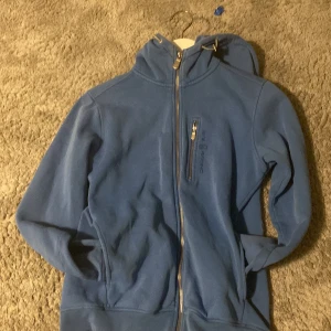 Blå fleecejacka från Sail Racing - Säljer en blå fleecejacka från Sail Racing i storlek XS. Jackan har en dragkedja framtill och en bröstficka med dragkedja. Perfekt för kyliga dagar med sin mjuka och varma insida.
