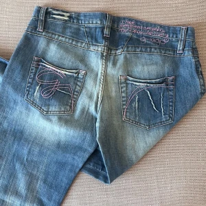 Lågmidjade Y2K-jeans - Superfina jeans med rosa sömmar och broderad text på baksidan. I mycket bra skick, se bilder 🙏💕 Midjemått: ca 40 cm Midjehöjd: ca 18 cm  Innerbenslängd: ca 80 cm  Passar tyvärr inte mig, så har inga bilder på. Tveka inte att skriva om du har frågor!🥰