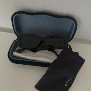 Svarta solglasögon från Gucci - Snygga svarta solglasögon från Gucci med en rektangulär form. De har en elegant och stilren design med Gucci-loggan på sidan. Perfekta för att ge en lyxig touch till din outfit. Kommer med originalfodral och putsduk.