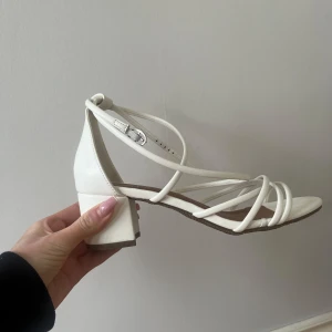 Vita klackar  - Stilrena vita klackar från Duffy. Sandalerna har en elegant design med en justerbar rem runt ankeln. Bara använda en gång. Nypris 600kr