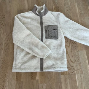 Vit fleecejacka från H&M med Snoopy-motiv - Säljer en mysig vit fleecejacka från H&M med ett stort Snoopy-motiv på ryggen. Perfekt för lite små kyliga vårdagar.