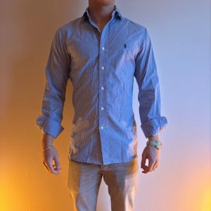 Blå rutig skjorta från Ralph Lauren - Snygg blå rutig skjorta från Ralph Lauren med klassisk krage och knappar framtill.. Perfekt för en stilren look.