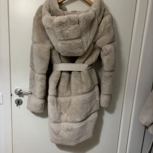 Beige pälsjacka från Amisu - Säljer en supermjuk och fluffig beige pälsjacka från Amisu. Jackan har en lång design med ett bälte i midjan och en stor huva för extra mysfaktor. Köpte för 599 men säljer för 450🧥✨knappt använt 