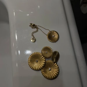 Hängande örhängen med tillhörande armband - Snygga guldörhängen med en unik cirkulär design. De har en räfflad yta och en liten glittrande detalj i mitten av varje cirkel. Perfekta för att ge en elegant touch till din outfit. Med tillhörande armband, helt oanvänt! Edblad