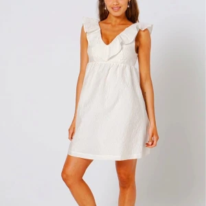 Studentklänning  - Söt vit studentklänning med volangdetaljer vid axlarna och en v-ringad hals. Klänningen är helt oanvänd med prislappen kvar på. Säljer eftersom jag köpte fel storlek💕💋🥰 Slutsåld på hemsidan.