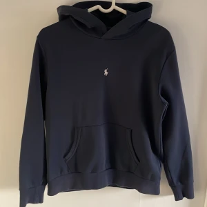 Mörkblå hoodie från Ralph Lauren - Säljer en stilren mörkblå hoodie från Ralph Lauren med det klassiska broderade logotypen på bröstet. Tröjan har en bekväm passform med långa ärmar och en praktisk magficka. Perfekt för en avslappnad look.                     Svarar snabbt på frågor!