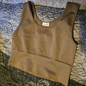 Brun ribbad linnetopp från Gymshark - Säljer en snygg brun ribbad linnetopp från Malene Birger. Den är ärmlös och har en tight passform, perfekt för träning eller en avslappnad dag. Materialet är mjukt och stretchigt, vilket gör den superbekväm att ha på sig.