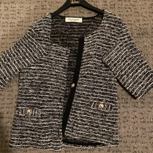 Svartvit kavaj från Oscar de la Renta - Säljer en elegant svartvit kavaj/kofta. Den har ett snyggt randigt mönster och långärmad. Kavajen är dekorerad med fina knappar framtill och vid fickorna. Perfekt för både vardag och fest!1knapp