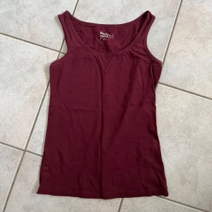 Vinröd linnetopp från Basic You - Säljer en enkel och stilren vinröd linnetopp från Basic You i storlek XS. Toppen är tillverkad av ekologisk bomull och är perfekt för en avslappnad vardagslook. Den är ärmlös och har en rund halsringning. skriv vid frågor💗