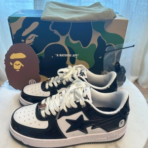 Bapesta svart, 41.5 - Helt nya Bapesta svart i storlek 42.5. Sko med en unik design som kombinerar BAPE:s ikoniska camo-mönster med Nikes klassiska Air Force 1. Skon har en svart glansig läderöverdel med vita detaljer. Skon levereras med original paket och tillbehör.
