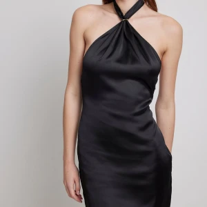 Svart halterneck klänning - Elegant svart halterneck klänning i satin med öppen rygg. Perfekt för en stilren look med en touch av glamour. Klänningen har en kort längd och en smickrande passform.