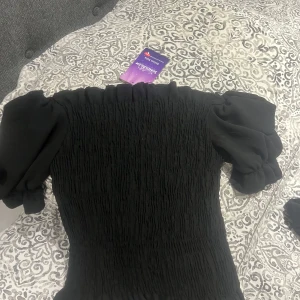 Svart smockad topp - Snygg svart smockad topp med puffiga korta ärmar. Perfekt för en stilren look. Toppen har en elastisk passform som ger en bekväm känsla.