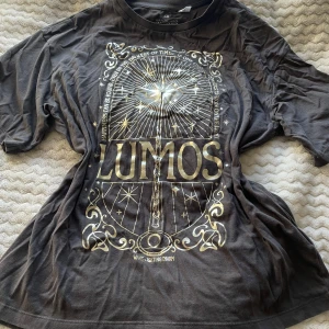 Grå t-shirt med Lumos-tryck från H&M - Säljer en cool grå t-shirt från H&M med ett stort Lumos-tryck i guld. T-shirten har korta ärmar och är perfekt för alla Harry Potter-fans. Den är gjord i mjuk bomull och har en avslappnad passform. Skriv gärna innan köp 😊