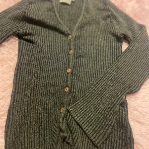 Grå ribbad kofta från Hennes Collection - Säljer en stilren grå ribbad kofta från Hennes Collection. Koftan har långa ärmar och knappar framtill, perfekt för lager på lager-stilen eller bara för sig. 