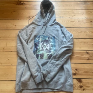Grå hoodie från Marcus & Martinus - Säljer en grå hoodie från Marcus & Martinus med tryck på framsidan. Tröjan har en justerbar huva med dragsko och långa ärmar. Perfekt för en avslappnad stil.