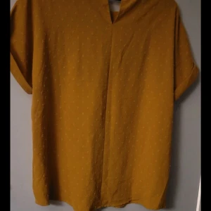 Gul blus med korta ärmar - Säljer en stilren gul blus med korta ärmar och diskret mönster. Blusen har en avslappnad passform och är perfekt för en bekväm och trendig look.