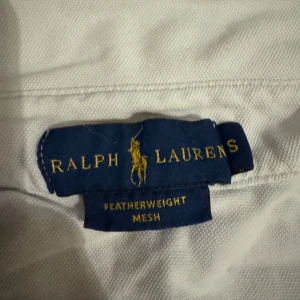 Vit skjorta från Ralph Lauren - Säljer en klassisk vit skjorta från Ralph Lauren i featherweight mesh. Skjortan har långa ärmar och knappar framtill. Loggan är broderad på bröstet i blått. Perfekt för en stilren look.