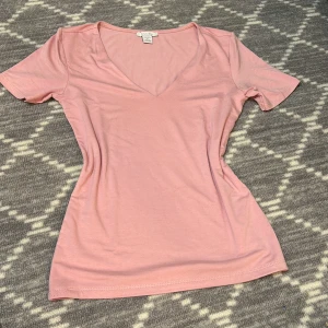 Rosa v-ringad topp från Amisu - Säljer en söt rosa v-ringad topp från Amisu. Toppen har korta ärmar och är tillverkad i ett mjukt material som känns skönt mot huden. Perfekt för en avslappnad stil. Aldrig använd