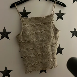 Beige ribbad linnetopp - Säljer en beige ribbad linnetopp med smala axelband. Toppen har en elastisk och bekväm passform som gör den perfekt för varma dagar. Den är stilren och lätt att matcha med olika outfits.