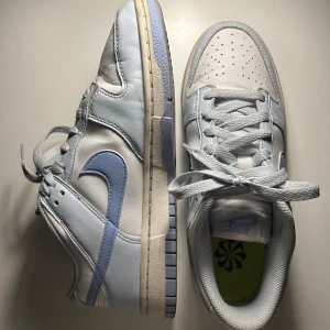 Nike Dunk i ljusblått och vitt - Snygga Nike Dunk sneakers i en fräsch kombination av ljusblått och vitt. Skorna har klassisk snörning och är bekväma. Säljer för att jag aldrig använder dem, bra skick endast använda fåtal gånger 