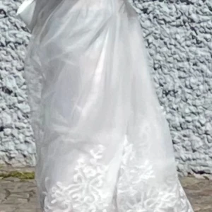 Barnklänning, brudnäbb  - Elegant vit långklänning med vackra broderade detaljer och stora rosetter. Klänningen har en romantisk känsla med sitt genomskinliga lager och fina spetsar. Perfekt för speciella tillfällen. Strl.114cm lång, från axel till tå. 62 cm midja, mätt rakt över sida till sida. Använd en dag vid bröllop. Det finns möjligen en till i samma storlek att tillgå. Strl.30 kan vara fel angiven storlek på de val man gör inför annonsen. 