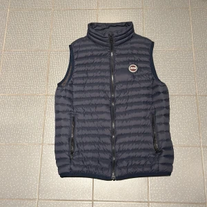 Mörkblå dunväst från Colmar - Snygg mörkblå dunväst från Colmar med dragkedja och hög krage. Västen har ett stilrent quiltat mönster och två praktiska fickor med dragkedja. Perfekt för kyligare dagar. Skick 8,5/10, fel på en sömn, bild 5. 