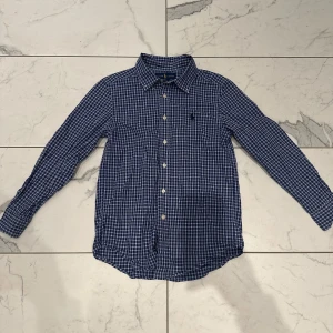 Blå rutig skjorta från Ralph Lauren - Säljer denna snygga blå rutig skjorta från Ralph Lauren med klassisk krage och knappar framtill. Skjortan är i skick 8/10 och i  storlek 10-12 år! Orginal pris - 1100kr Vårat pris - 149kr. Priset är inte hugget i sten! Skriv vid minsta lilla fundering!🙌