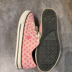 Rosa Converse med stjärnmönster - Säljer ett par rosa Converse sneakers med ett coolt stjärnmönster. Skorna har vita snören och en klassisk vit sula med svart rand. Supersnygga!! 