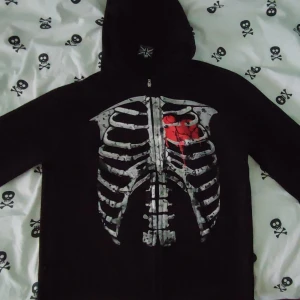 Skelett Zip-Up  - Snygg och unik huvtröja med tryck av revben och hjärta. Dragkedja framtill. Tröjan är i svart med ett iögonfallande tryck. Perfekt för den som vill sticka ut! Fick hem den idag då den var köpt av någon annan på Vinted, provade den och så passade den inte tyvärr. Kände att istället för att skänka den eller slänga så kanske någon annan får bättre användning. För mig så sitter den som ett S-XS. Den är liten i storleken kan man säga. Skriv för fler bilder och frågor tack! :D
