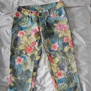 Blommiga byxor från Italien - Snygga blommiga byxor med tropiskt mönster i grönt, rosa och blått. Tillverkade i Italien, dessa byxor har en normal passform och är perfekta för en färgglad stil. De har knappar och dragkedja framtill. Lite stretchiga.Aldrig använd.Midjan 37cm×2
