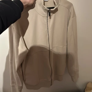 Beige tröja från Calvin Klein - Säljer en stilren beige tröjan från Calvin Klein med dragkedja och ribbade detaljer. Tröjan har en broderad logga på kragen och är långärmad. Perfekt för en avslappnad look. Tröjan är i helt nytt skick då den är bara använd 1-2 gånger. Köpt på boozt för 899kr för ett år sen.