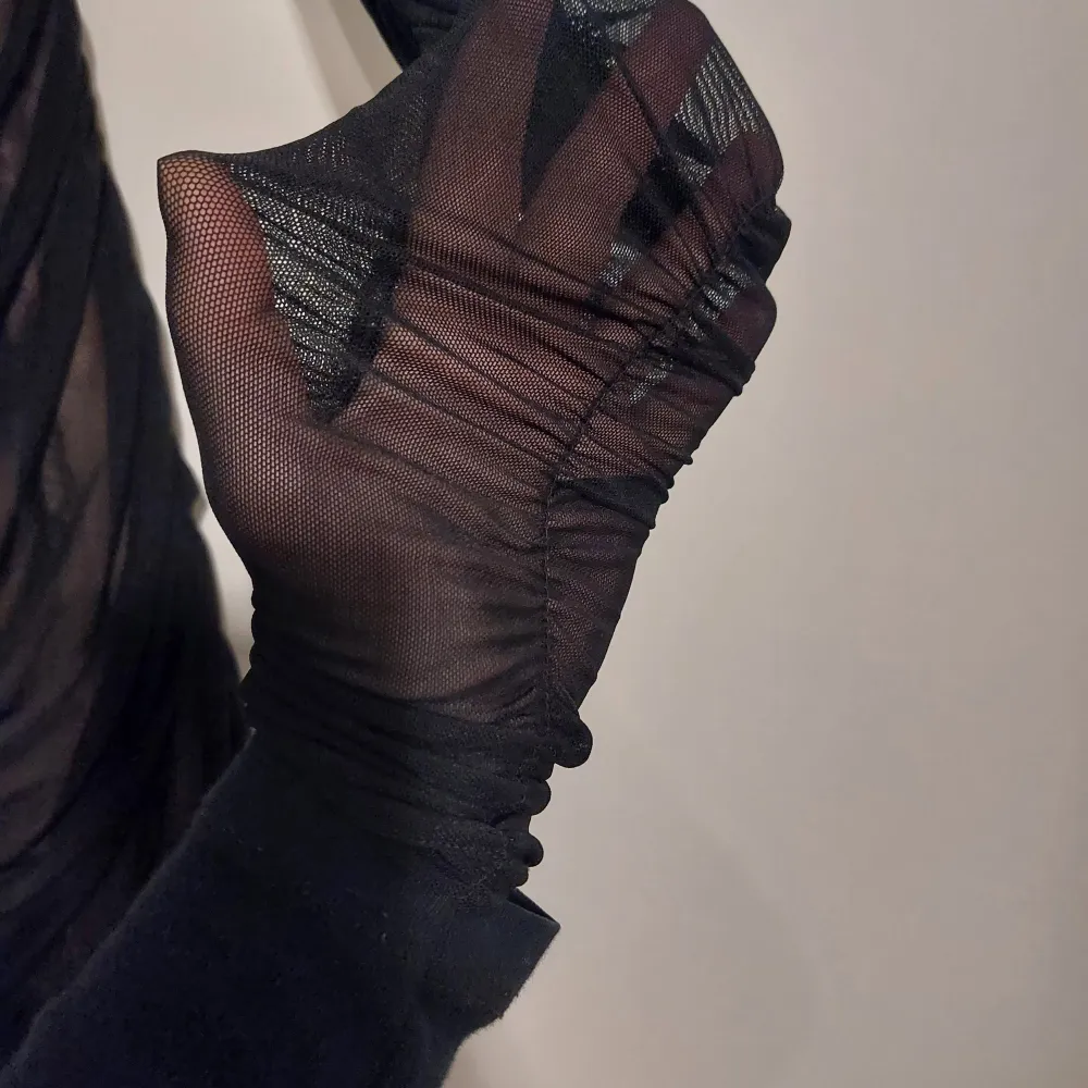 Snygg svart offshoulder klänning med transparenta detaljer och rynkad design. Klänningen har långa ärmar och en figurnära passform som ger en elegant look. Perfekt för en kväll ute eller en speciell tillställning.. Mekot.