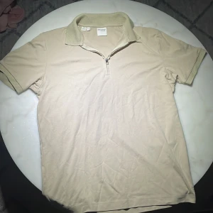  pikétröja  - Säljer en stilren beige pikétröja från Selected Homme. Tröjan har en dragkedja vid halsen och korta ärmar. Perfekt för en avslappnad och snygg look. 