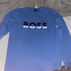 Blå tröja från Boss - Snygg blå tröja från Boss med stort tryck på bröstet. Tröjan har långa ärmar och en rund halsringning. Perfekt för en avslappnad stil.