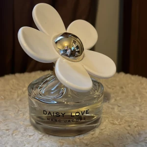 Daisy Love parfym från Marc Jacobs - Säljer en Daisy Love parfym från Marc Jacobs. Flaskan har en unik design med en stor vit blomma på toppen och en rund, genomskinlig glasflaska. Perfekt för den som älskar en fräsch och blommig doft. Parfymen är 100ml från början och jag har använt ungefär hälften så jag skulle väl säga att det är 50ml kvar då😍😍Säljer då jag tröttnat på doften