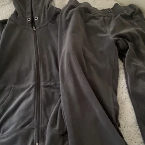 Grå hoodie och byxor set - Mysigt set med en grå hoodie och matchande byxor. Hoodien har dragkedja och en praktisk huva med snörning. Perfekt för en avslappnad dag hemma eller ute på stan. Hoodien är i storlek M och byxorna är L