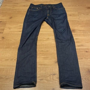 Mörkblå slimfit jeans från Nudie Jeans - Snygga mörkblå jeans från Nudie Jeans med klassisk kontrastsömmar. De har en slim passform och är i raw denim. ytterst lite slitage i grenen men ej hål eller något man märker. använda runt 8 gånger och tvättade 1 gång. skriv innan du vill köpa