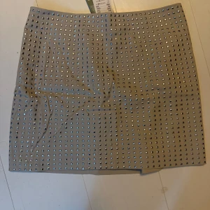 Beige kjol med nitar - Trendig beige kjol dekorerad med glänsande nitar över hela ytan. Perfekt för att ge en edgy touch till din outfit. Kjolen har en rak passform och är knälång.