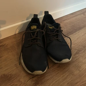 Mörkblåa sneakers från G-Star RAW - Säljer ett par mörkblå sneakers från G-Star RAW. Skorna har en stilren design med snörning och en vit sula som ger en snygg kontrast. Perfekta för en avslappnad stil.